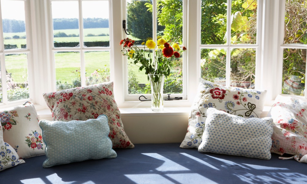 blue cushioned seating with floral pillows under a white window overlooking a North Carolina backyard