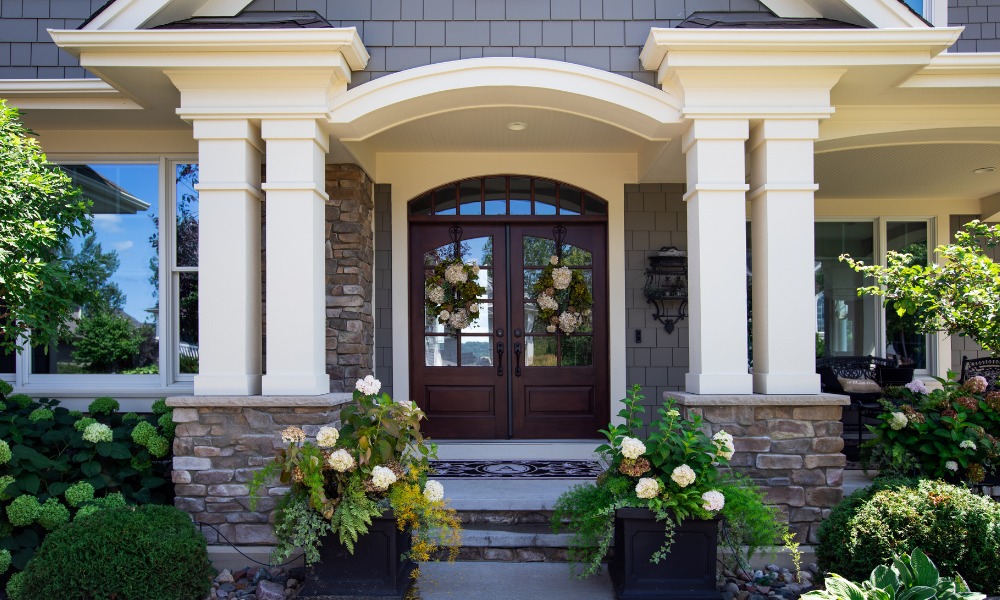 A craftsman style front porch with double columns either side of the front door, potted hydrangeas, and an arch-top wood double door with 3/4 light